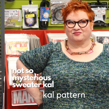 Load image into Gallery viewer, Kim, a redheaded white woman, wearing Bumblebee,  a speckled green, blue and teal short sleeve sweater in a record store.
